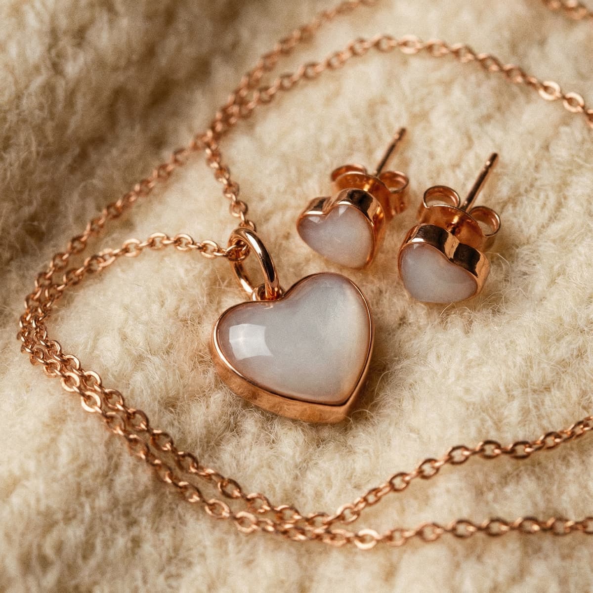 Rose gold heart pendant necklace and matching heart stud earrings with milky white resin, a sentimental weaning gift displayed on a soft cream wool background.