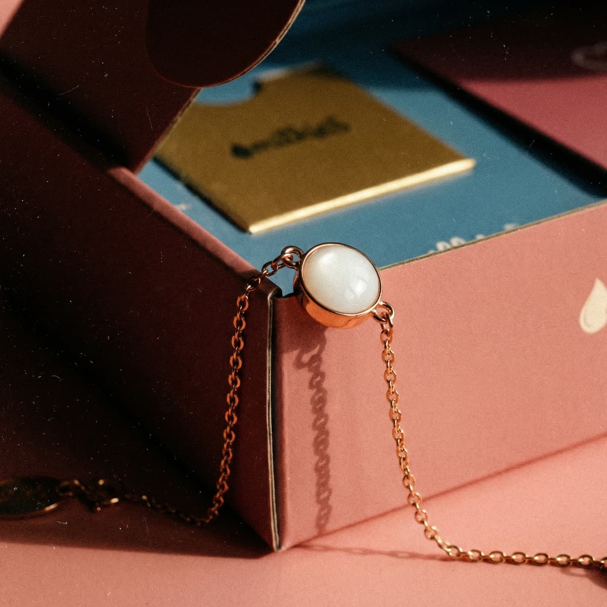 Gold chain bracelet with a round white resin keepsake stone displayed on pink packaging, representing a breastmilk bracelets diy making kit result.
