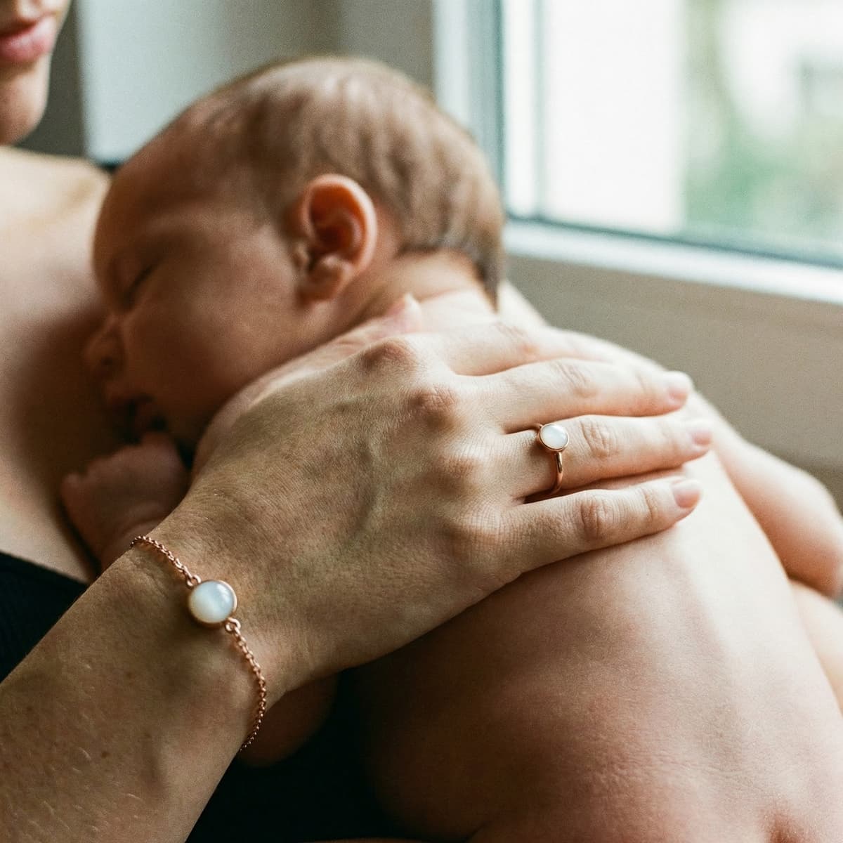 Mother cuddling a sleeping newborn while wearing a breastmilk bracelet and ring, showing why a breastmilk bracelets diy making kit is a meaningful at-home keepsake for moms who want a private, hands-on way to preserve their breastmilk.