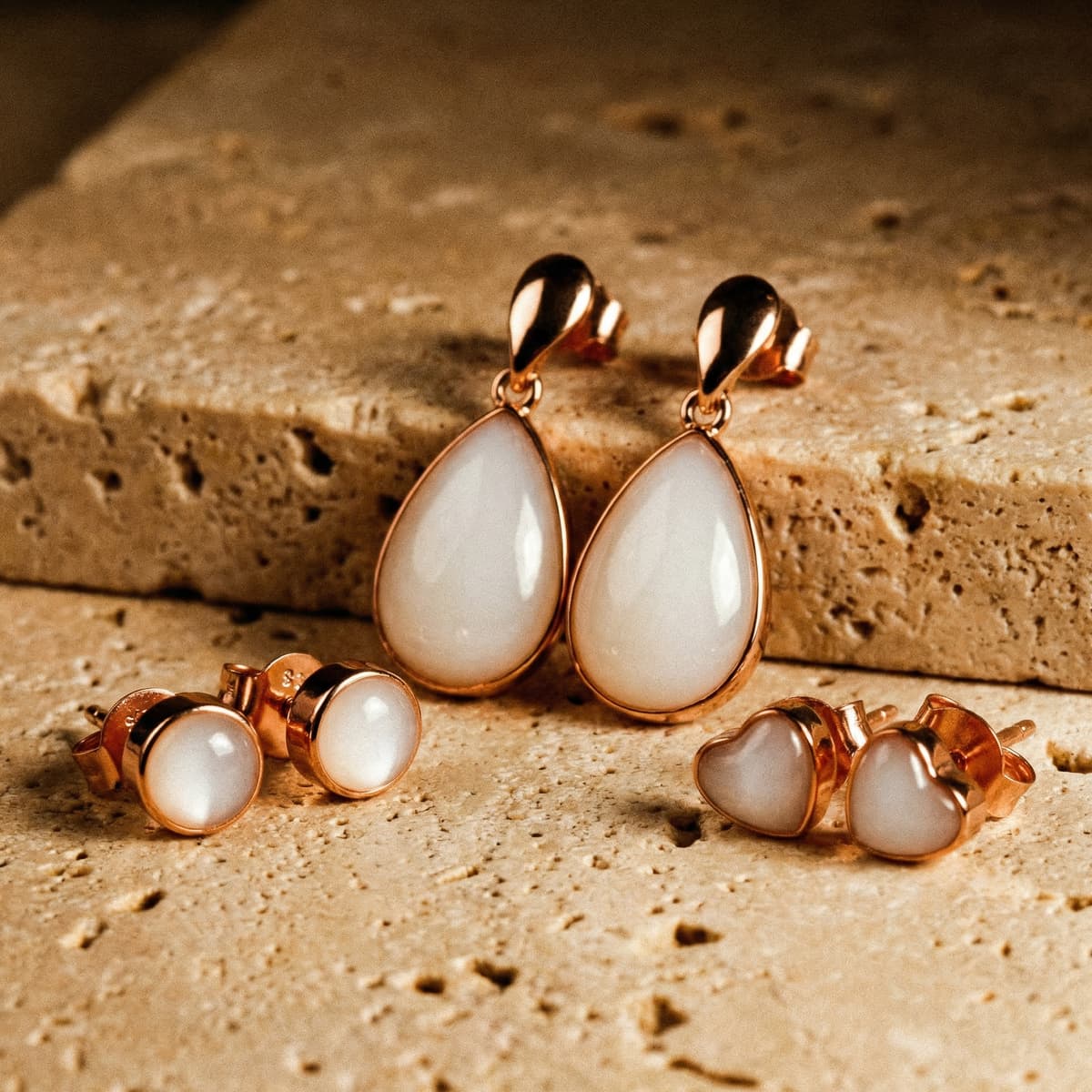 Rose gold teardrop dangle earrings with milky white resin stones on a textured beige background, representing keepsake jewelry made using a breastmilk earring diy making kit.