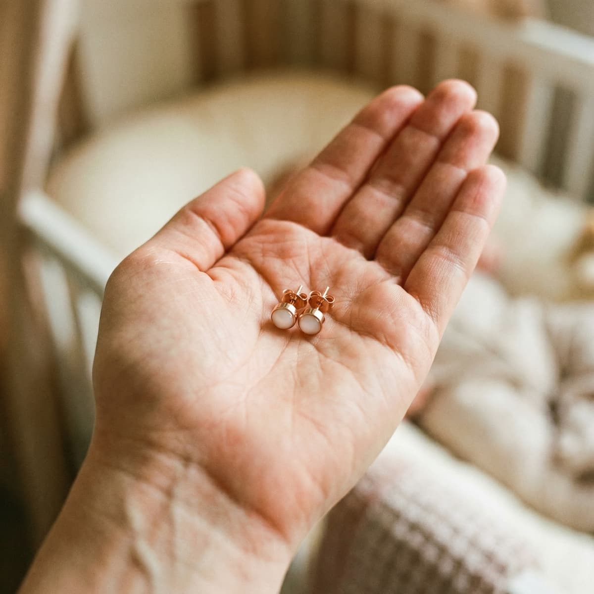 Rose gold stud earrings with milky white resin stones held in a hand, featuring a breastmilk earrings diy making kit keepsake in a soft nursery setting.