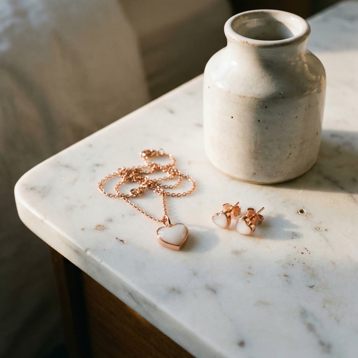 Rose gold heart pendant necklace and matching stud earrings with milky white inlays on a marble surface beside a ceramic vase, finished keepsakes made with a breastmilk jewellery diy kit.