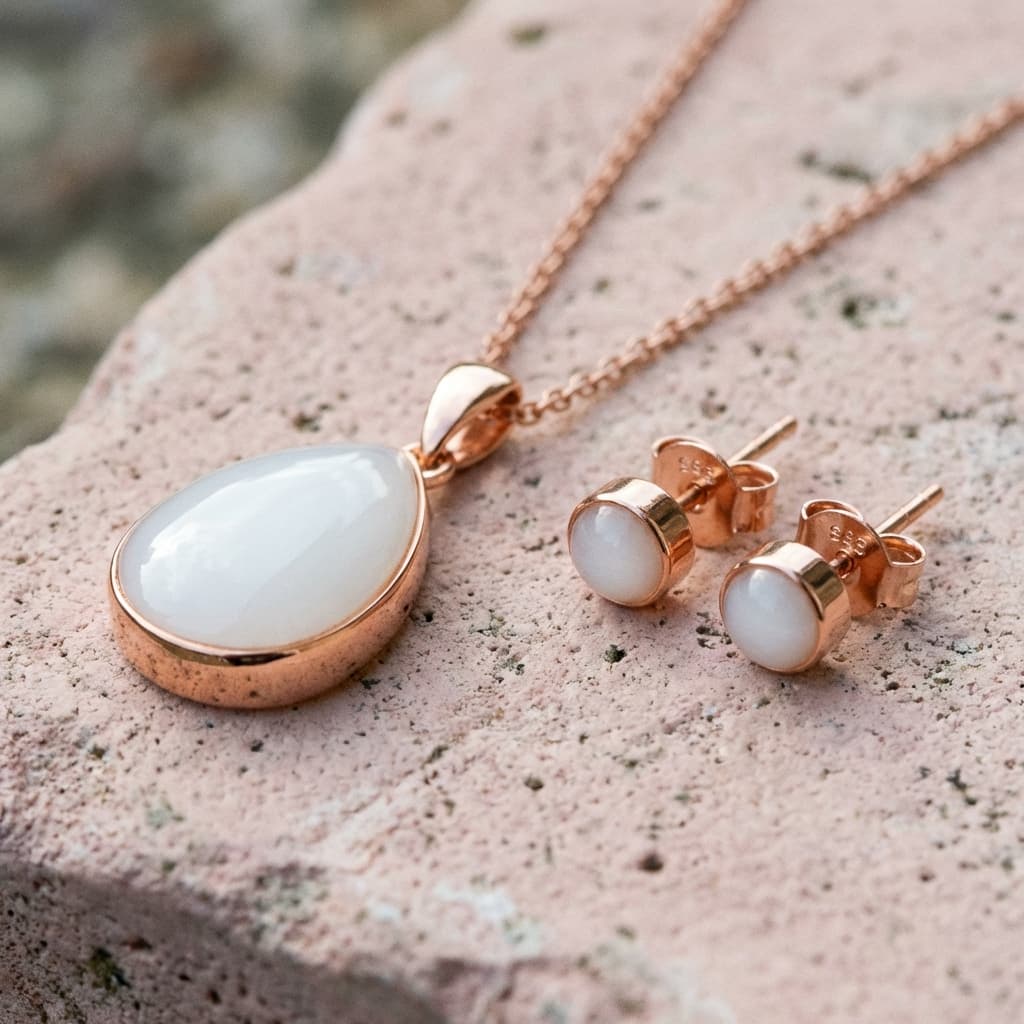 Handmade rose gold necklace pendant and matching stud earrings with milky white resin stones, created using a breastmilk jewelry diy kit, displayed on a textured stone background