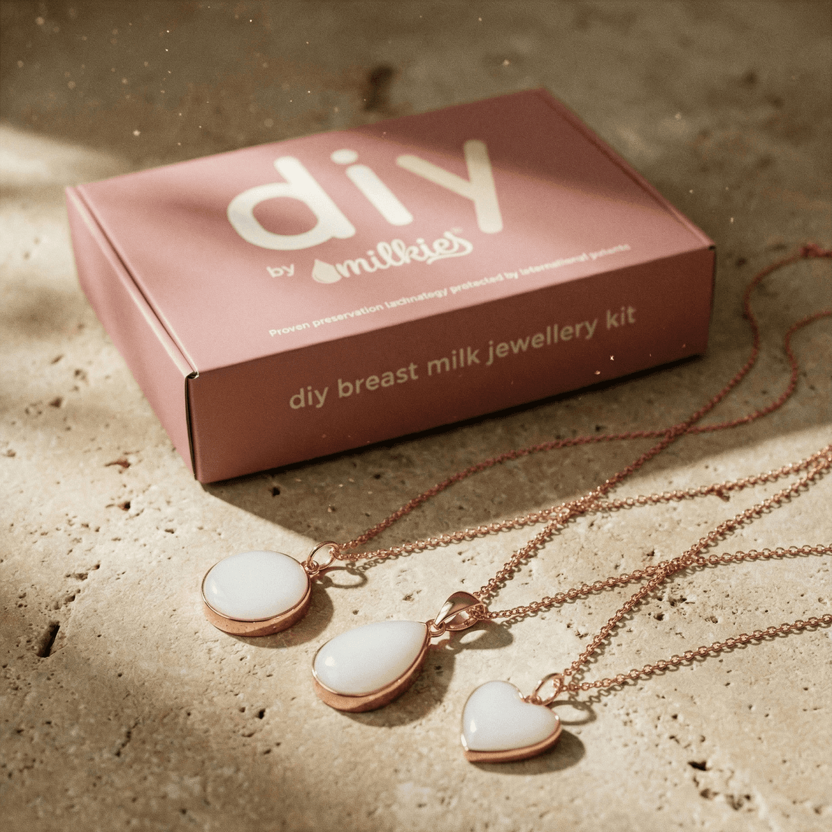 Rose-gold chain pendants and resin keepsake charms in round, teardrop, and heart shapes displayed on a stone surface from a DIY by MILKIES breastmilk necklaces making kit box.