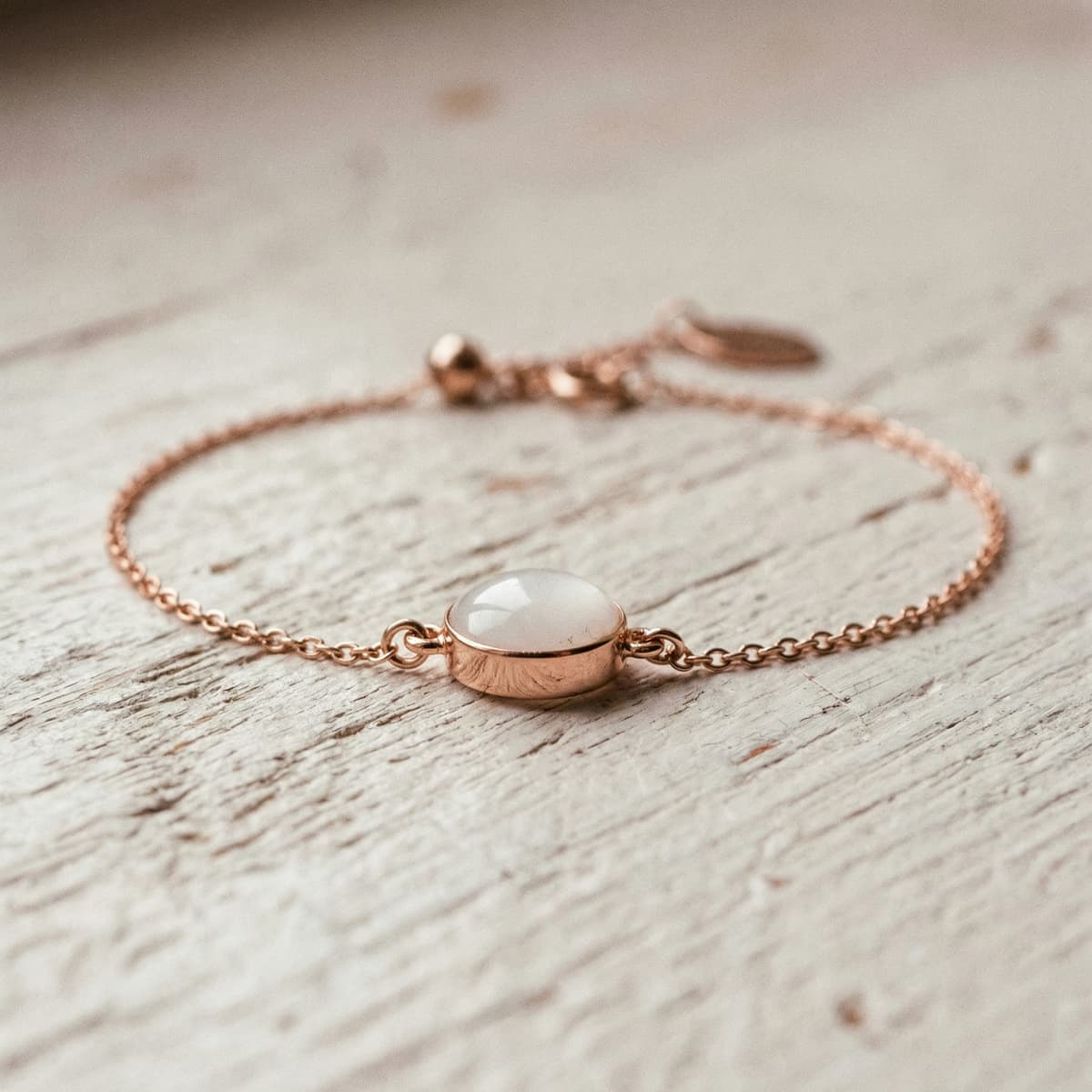 Rose gold chain bracelet with a milky white resin gemstone centerpiece, made using a diy breastmilk bracelet making kit, on a light wooden surface.