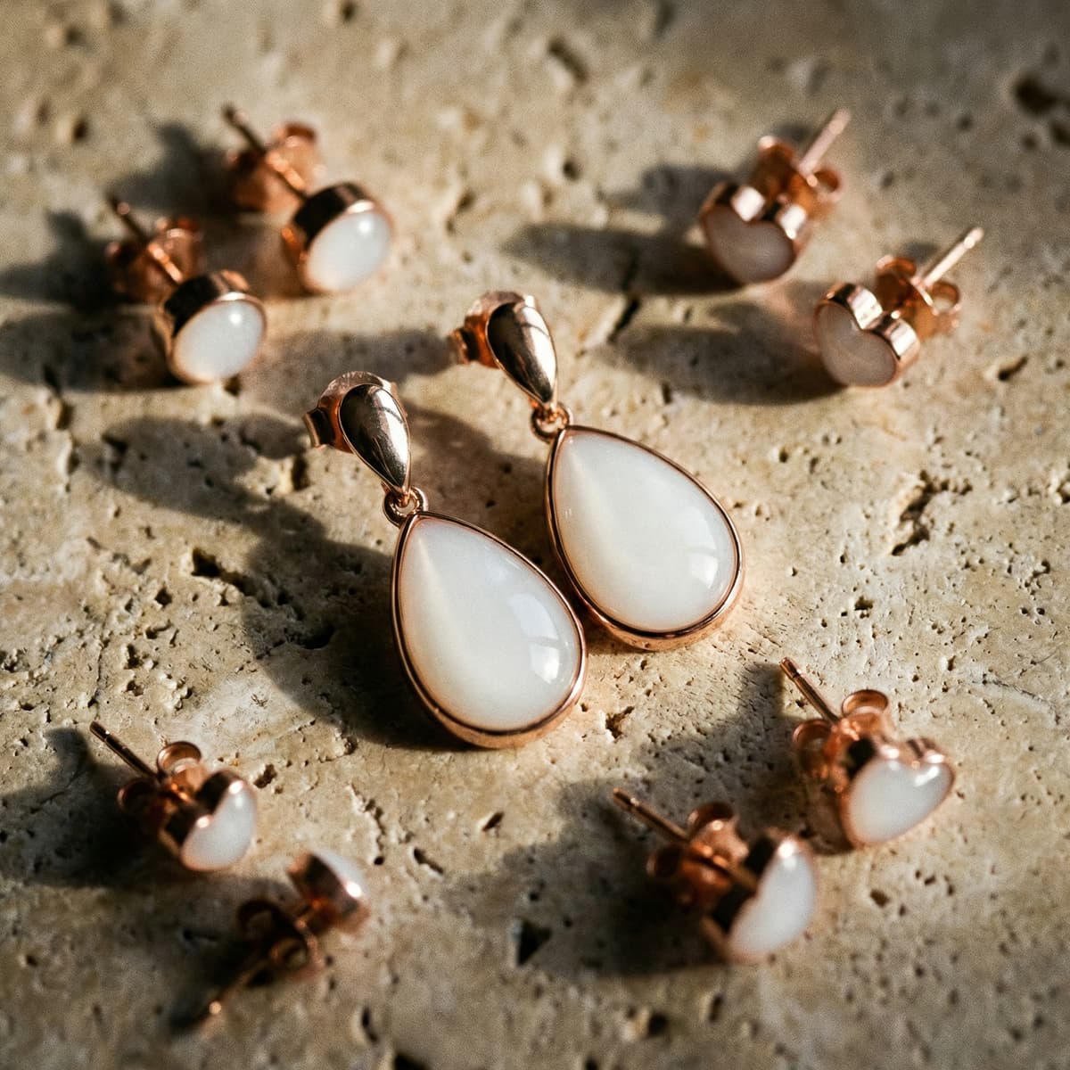 Rose gold breastmilk keepsake teardrop dangle earrings with heart stud settings displayed on a textured stone surface, made with a diy breastmilk earring making kit.