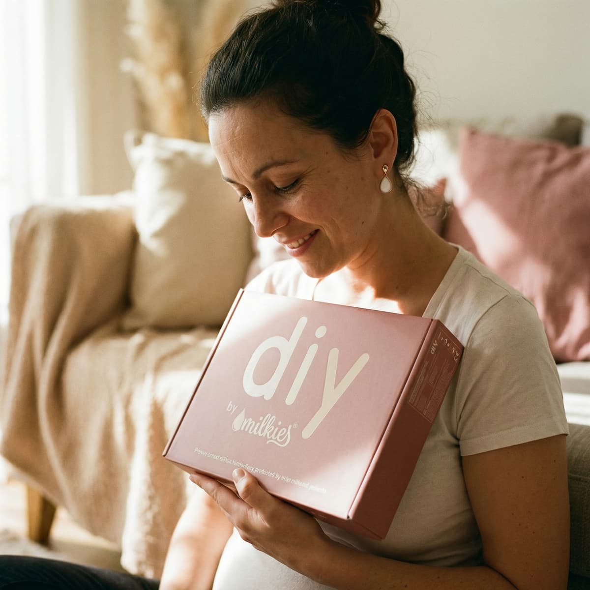 Smiling mom at home holding a DIY by MILKIES box, showing why a diy breastmilk earring making kit is an easy, private way to create a meaningful keepsake.